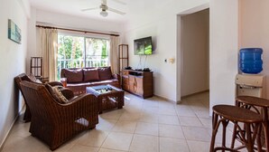 A living room with a sofa, chairs, a coffee table, a television, a water dispenser, and a ceiling fan. - Alicia Beach, Hispanola Sol! (Sosúa)