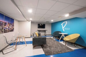 Ein moderner Arbeitsraum mit blauer Akzentwand, einem grauen Sofa, einem gelben Sessel, einem Glastisch und einem Wand-Fernseher.