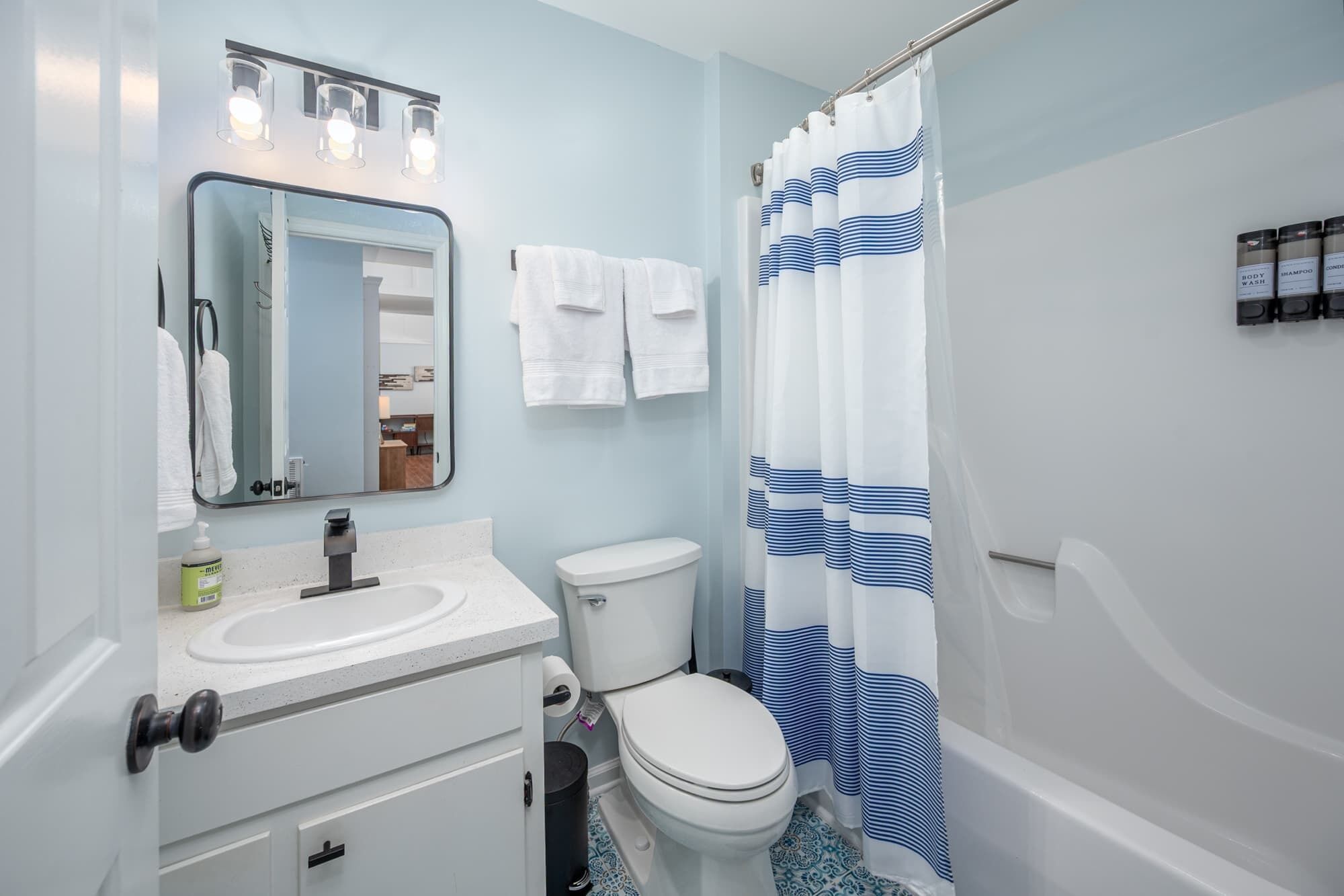 A bathroom with a white sink, a toilet, a mirror, and a shower curtain with blue stripes.