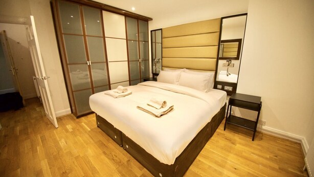 A bedroom with a wooden bed, a wardrobe with sliding doors, a bedside table, and a mirror. - Stylish flat in Oxford Circus (Londra)