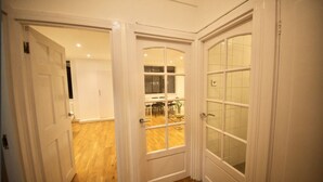 A hallway with white doors leading to a dining area with a wooden floor and a view of the outside. - Stylish flat in Oxford Circus (Londra)