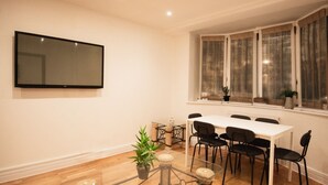 A dining area with a table and chairs, a TV mounted on the wall, and a window with curtains. - Stylish flat in Oxford Circus (Londra)