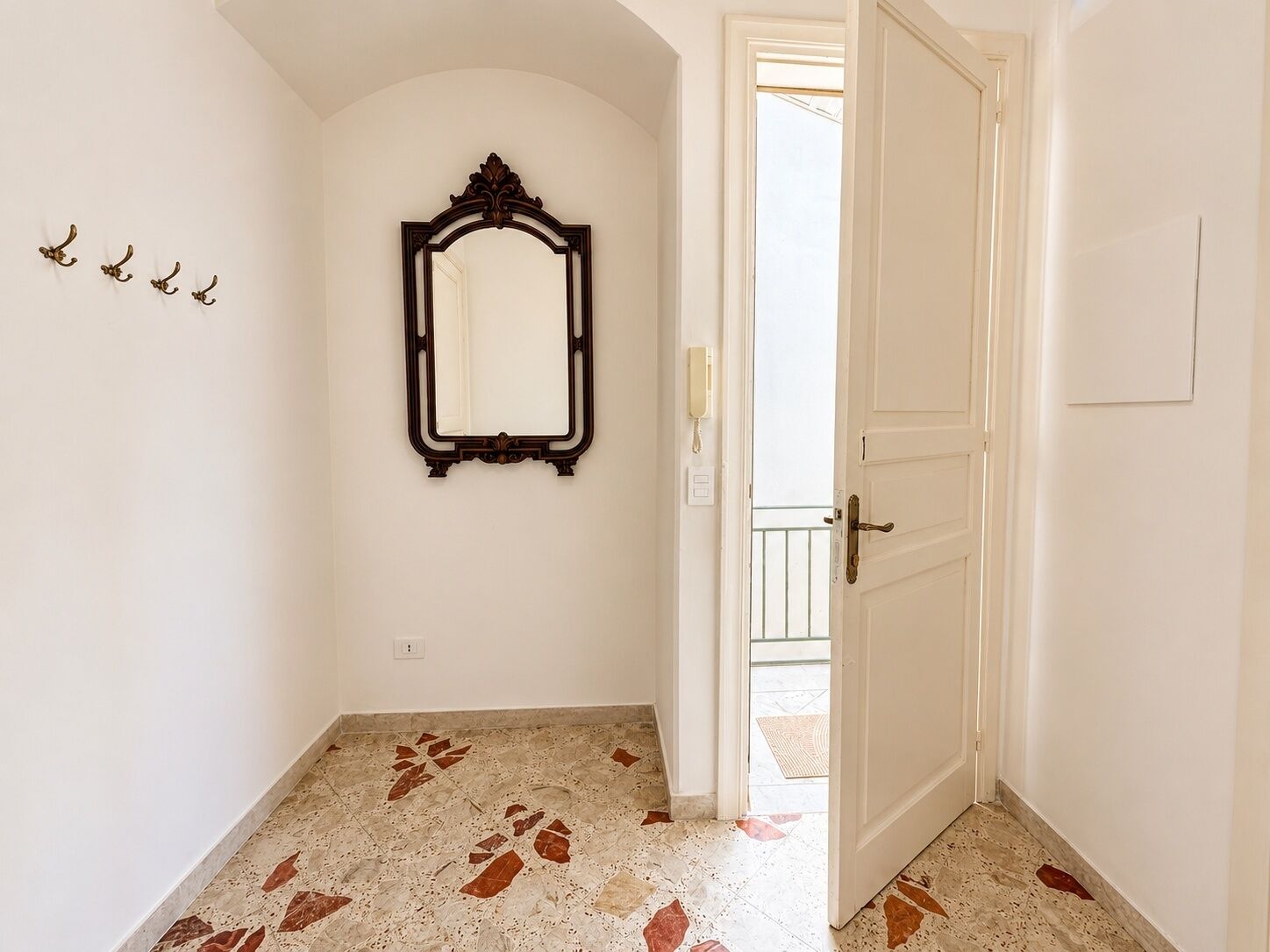 Un corridoio con pavimento in marmo, una porta e uno specchio fissato alla parete.