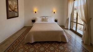 Ein Schlafzimmer mit einem Bett, zwei Wandleuchten, einem großen Fenster mit Vorhängen und einem gemusterten Boden.