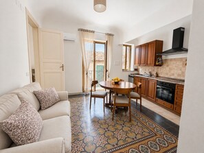 Un ambiente compatto con divano, tavolo da pranzo, sedie, angolo cottura con mobili in legno e pavimento decorato.