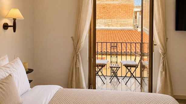 Ein Hotelzimmer mit Bett, Nachttisch, Lampe, Balkon mit Stühlen und Fernseher.