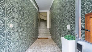 Un corridoio con piastrelle verde e bianche a motivi decorativi, una scala e un vaso bianco con piante verdi.
