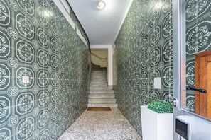 Ein Flur mit gemusterten, grün-weißen Fliesen, einer Treppe und einem weißen Blumentopf mit Grünpflanzen.