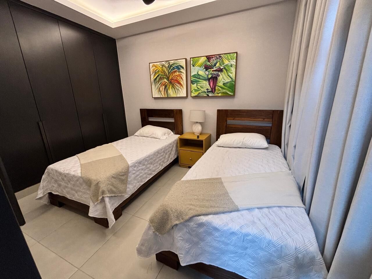 Una habitación de hotel con dos camas, una mesita de noche y dos cuadros colgados en la pared.
