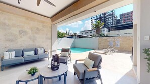 A modern outdoor living area with a pool, seating, and a view of a construction site. - Exclusivo zona A (Santiago de los Caballeros)