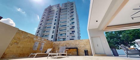 Un edificio moderno con piscina, sillas de descanso y vistas a un edificio residencial alto.
