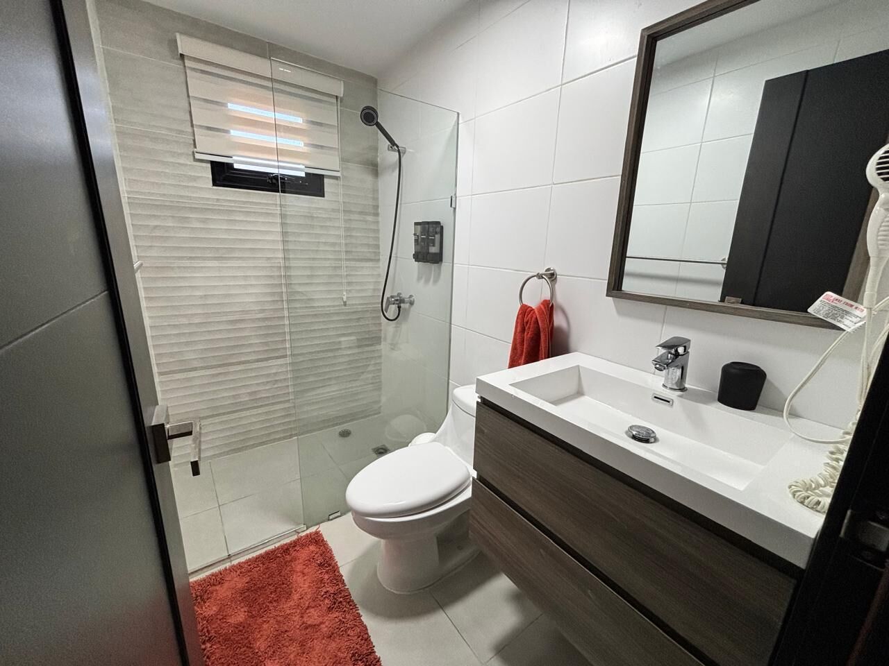 A modern bathroom with a glass shower enclosure, a white toilet, a white sink with a dark countertop, and a mirror above the sink.