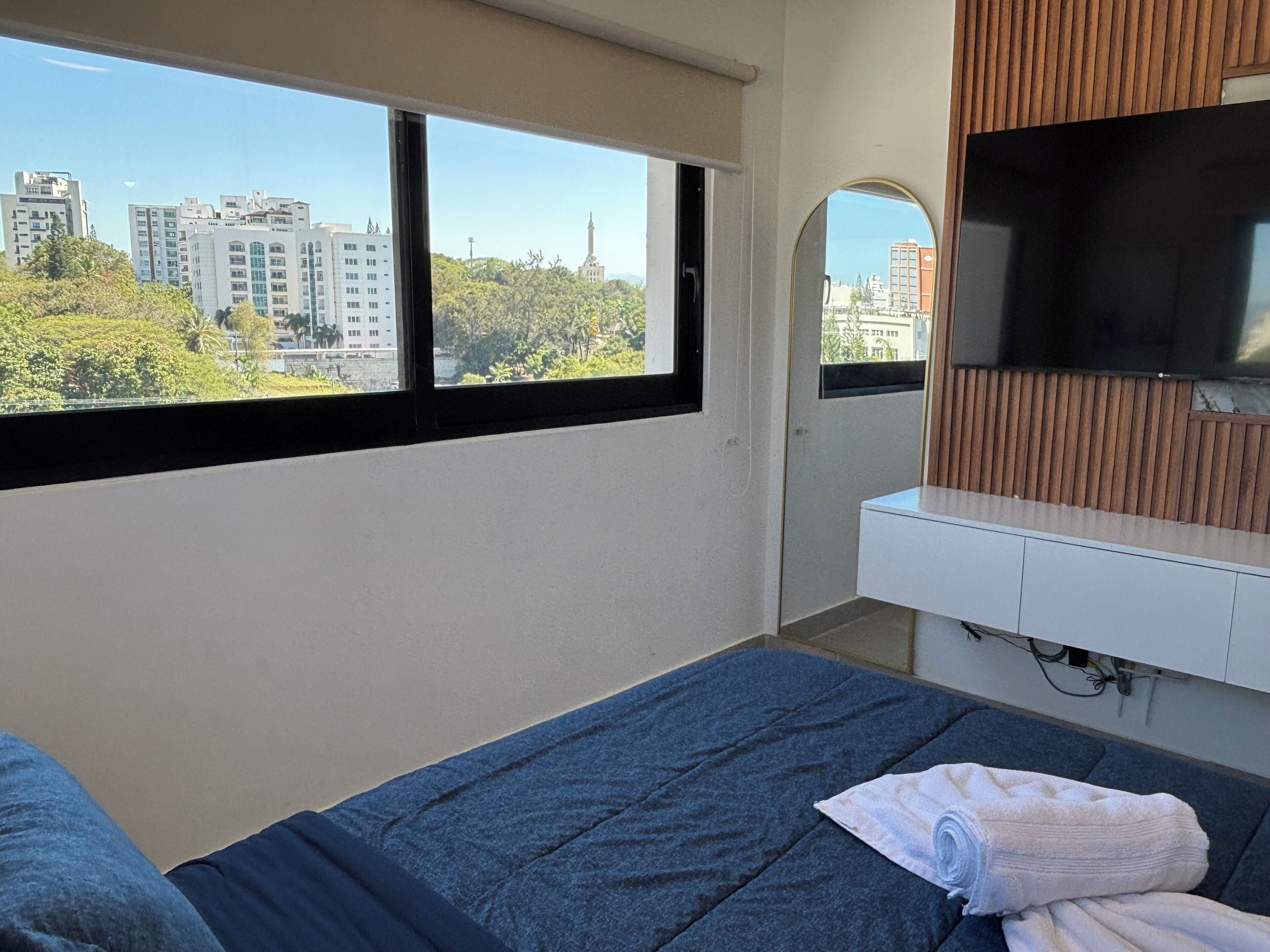 Ein Hotelzimmer mit einem Bett, einem Fernseher, einer Wand aus Holzpaneelen und einem Fenster mit Blick auf die Stadt.