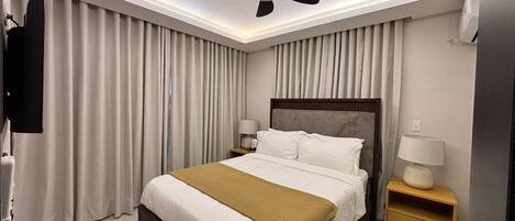 Een moderne hotelkamer met een bed, plafondventilator, bedlampen en een televisie.