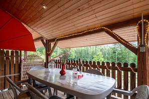 A wooden deck with a table set for dining, surrounded by a wooden fence, and a view of greenery in the background.
