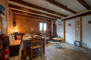 Ein gemütliches Blockhaushaus-Interieur mit Holzbalkendecke, einer Essecke mit Tisch und Stühlen, einer Couch, einem Kamin und einer Tür zu einer rustikalen Steinwand.