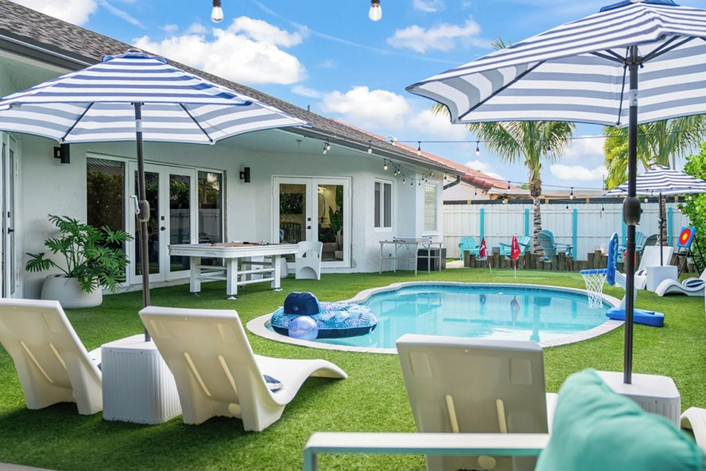 A backyard with a swimming pool, lounge chairs, and umbrellas.