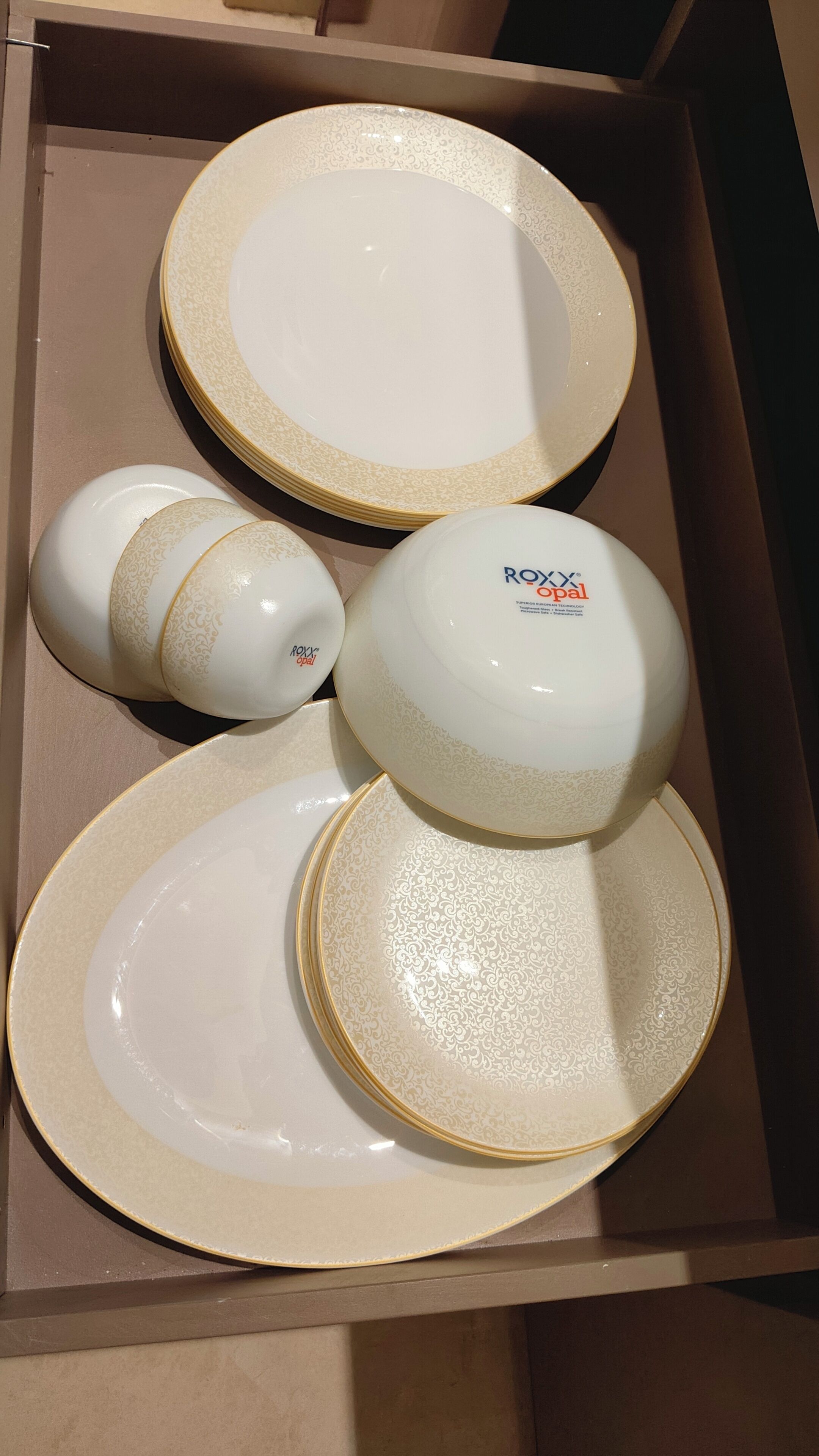 Una caja que contiene un juego de vajilla blanca con detalles dorados y un logotipo.