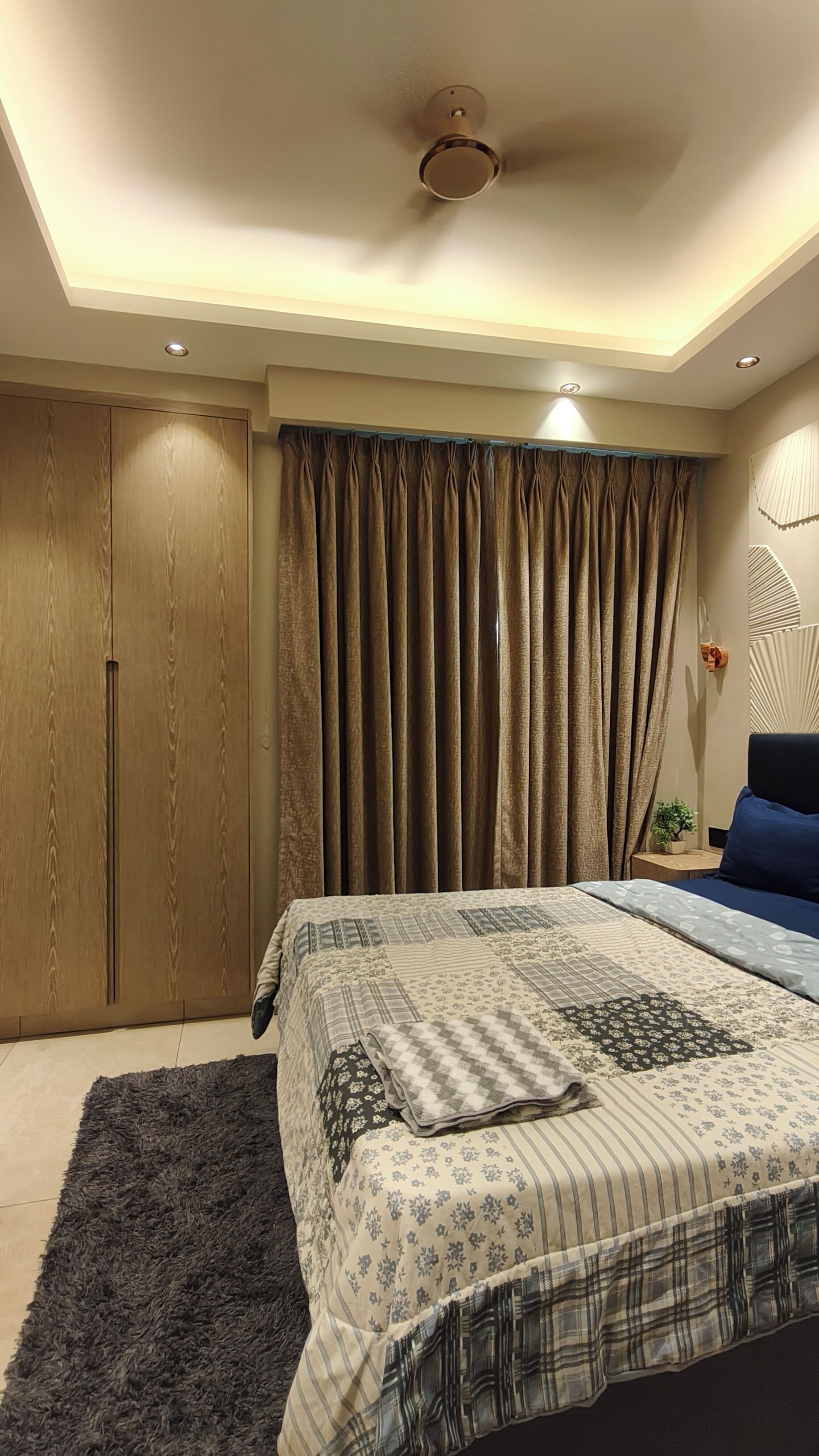 A bedroom with a bed, a wardrobe, a ceiling fan, and a window with curtains.
