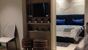 A modern room with a bed, a TV, a chair, and a small table.