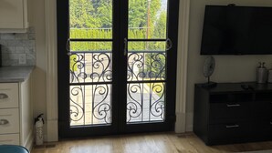 A room with a large arched door, a flat-screen TV, a wooden floor, and a kitchen area with white cabinets. - Chateau Calcaire Carriage House (Kelowna)
