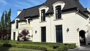A large, two-story house with a dark roof, white exterior walls, and a well-maintained front yard. - Chateau Calcaire Carriage House (Kelowna)