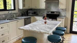 A kitchen with white cabinets, a marble island, and three bar stools. - Chateau Calcaire Carriage House (Kelowna)