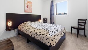 Ein Schlafzimmer mit Bett, Stuhl, Nachttisch, Lampe, Fenster und einem Bild an der Wand.