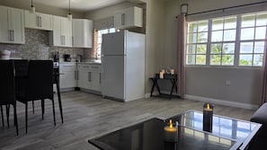 A modern kitchen with white cabinets, a refrigerator, and a dining area with a glass table and chairs.