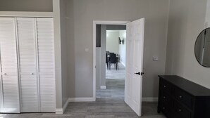 Un corridoio con un armadio chiuso, una porta aperta che dà su una sala da pranzo e un comò.