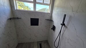 Un bagno con pareti in marmo, una finestra, una doccia e uno scaffale nero.