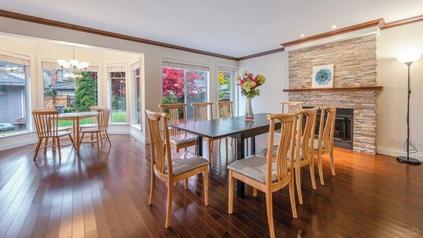 A dining area with a wooden table and chairs, a stone fireplace, and large windows with a view of a garden. - Comfortable Room in a Shared Home (Vancouver)