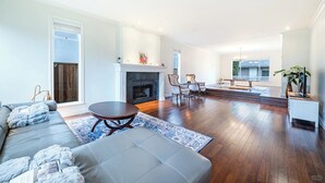 A spacious living room with a fireplace, a sofa, a coffee table, and a dining area with chairs. - Comfortable Room in a Shared Home (Vancouver)