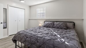 Een slaapkamer met een bed, een deur, een raam en een lamp.