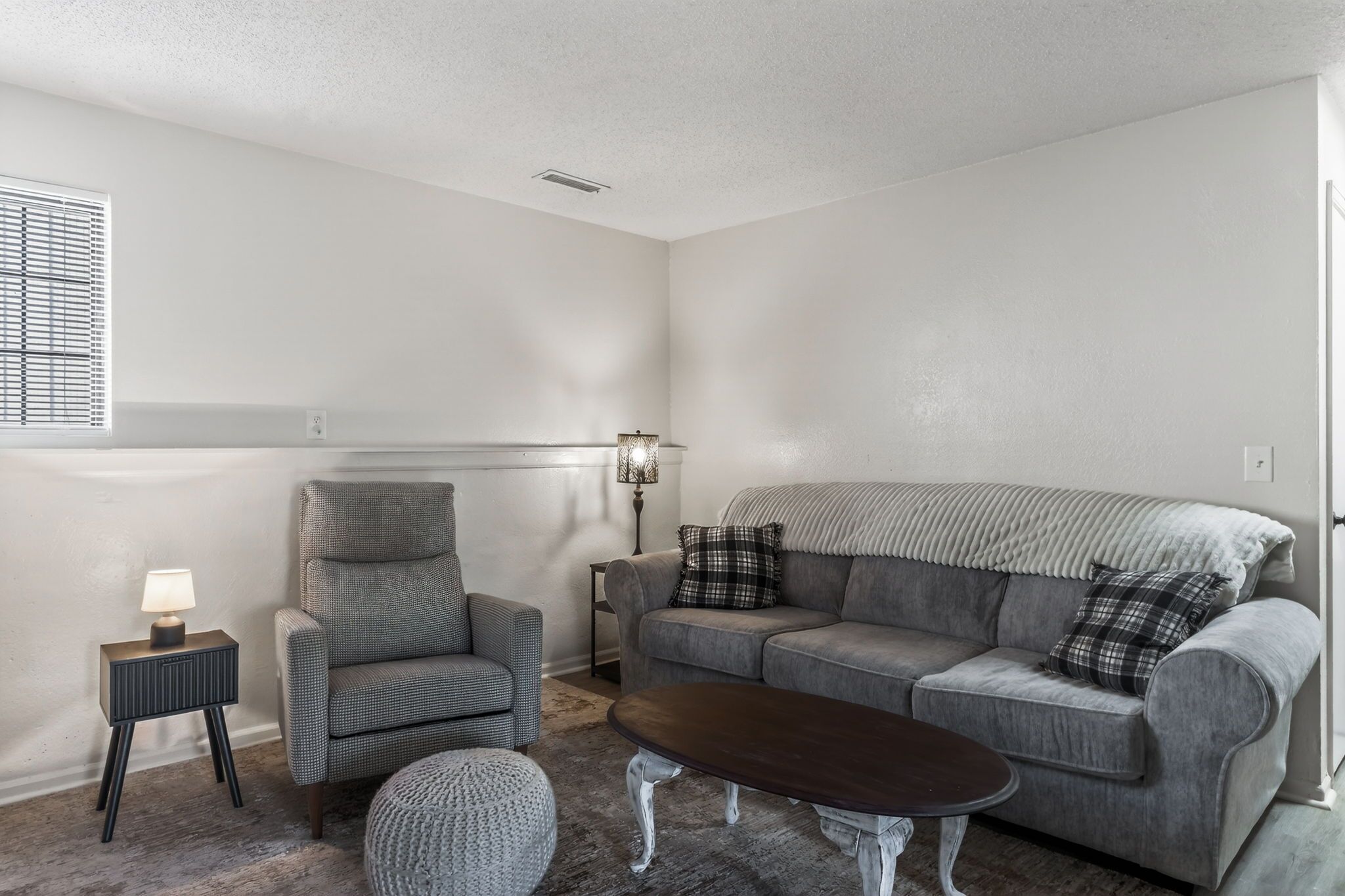 Ein Wohnzimmer mit grauem Sofa, einem kleinen Sessel, einem Couchtisch, einer Lampe und einer Heizung.