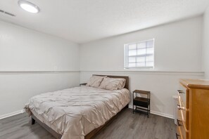 A bedroom with a bed, a nightstand, a dresser, a window, and a ceiling light.