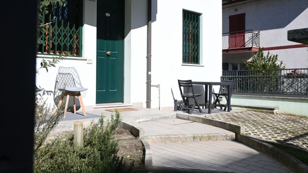 A courtyard with a green door, a small table with chairs, and a balcony with a railing. - RP03 - Cesenatico, new apartment near the sea (Cesenatico)