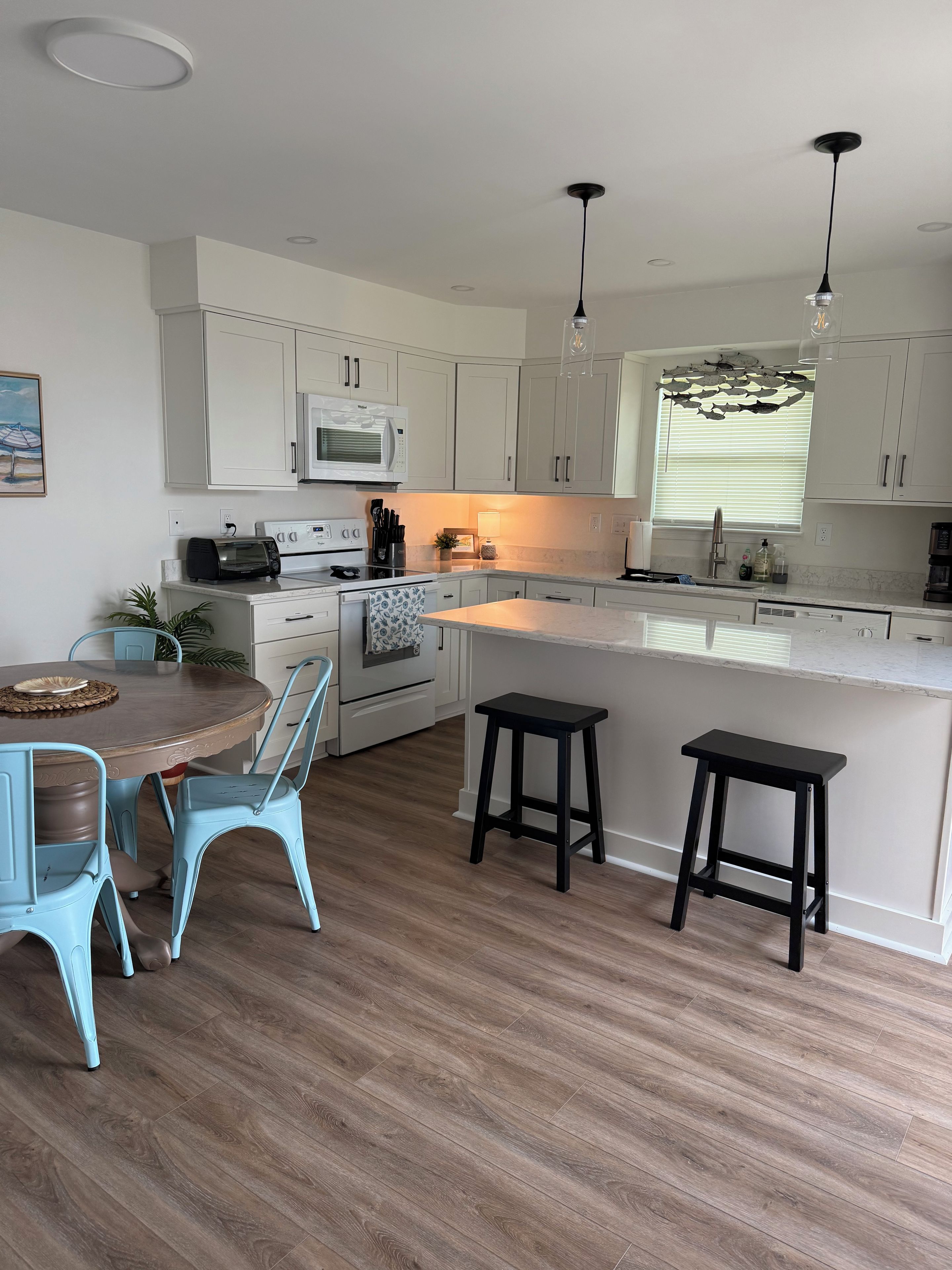 A modern kitchen with white cabinets, a central island, and a dining area with blue chairs.