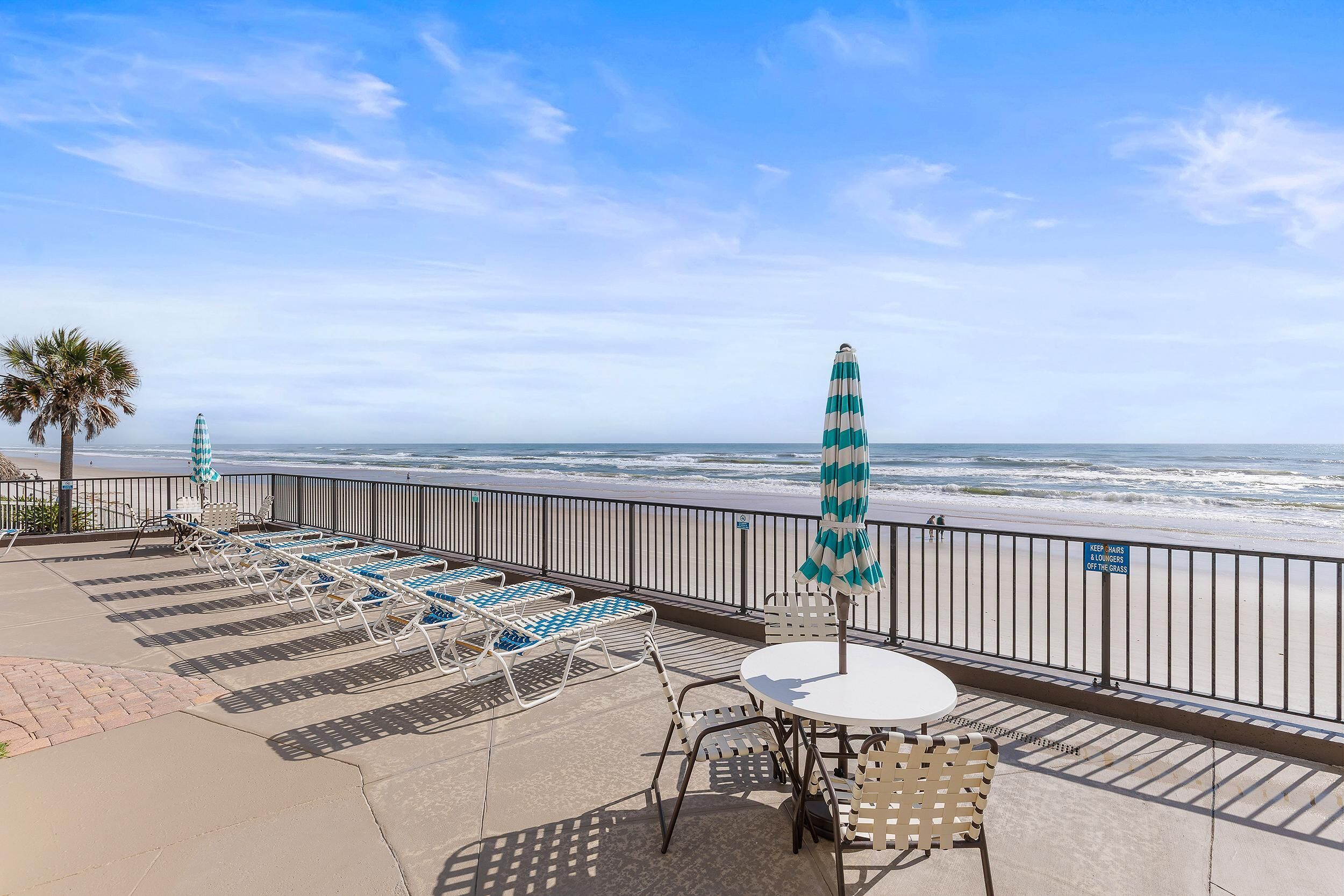 Un patio frente a la playa con sillones, una mesa y una sombrilla, con vista al océano.