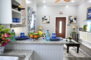 A kitchen with granite countertops, a sink, a dining area with a table and chairs, and a door leading to another room. - Cute as a Button, AC, Starlink, Wi-Fi, Hot Tub, Near Beaches, Bars & Restaurants (North Palmetto Point)