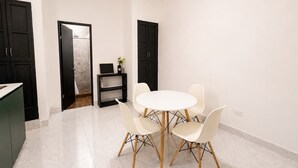 Un espace repas moderne avec une table ronde et six chaises, un meuble noir et une petite étagère ornée d’une plante.
