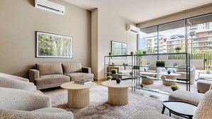 Un salón moderno con un sofá, mesas auxiliares redondas y una barandilla de cristal con vistas a una zona residencial.