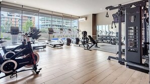 Un gimnasio con máquinas de cardio, equipo de levantamiento de pesas y ventanas amplias.