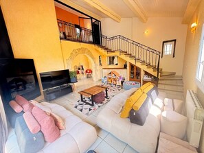 A spacious living room with a sofa set, a wooden coffee table, and a TV. A staircase with a railing leads to an upper level. - Dolce Villa, Pool and Comfort (Lattes)