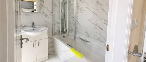 A bathroom with a marble wall, a glass-enclosed shower, a sink, and a mirror.