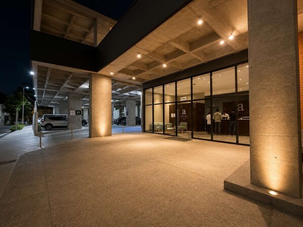 Un edificio moderno con fachada de vidrio, una recepción y un estacionamiento con automóviles.