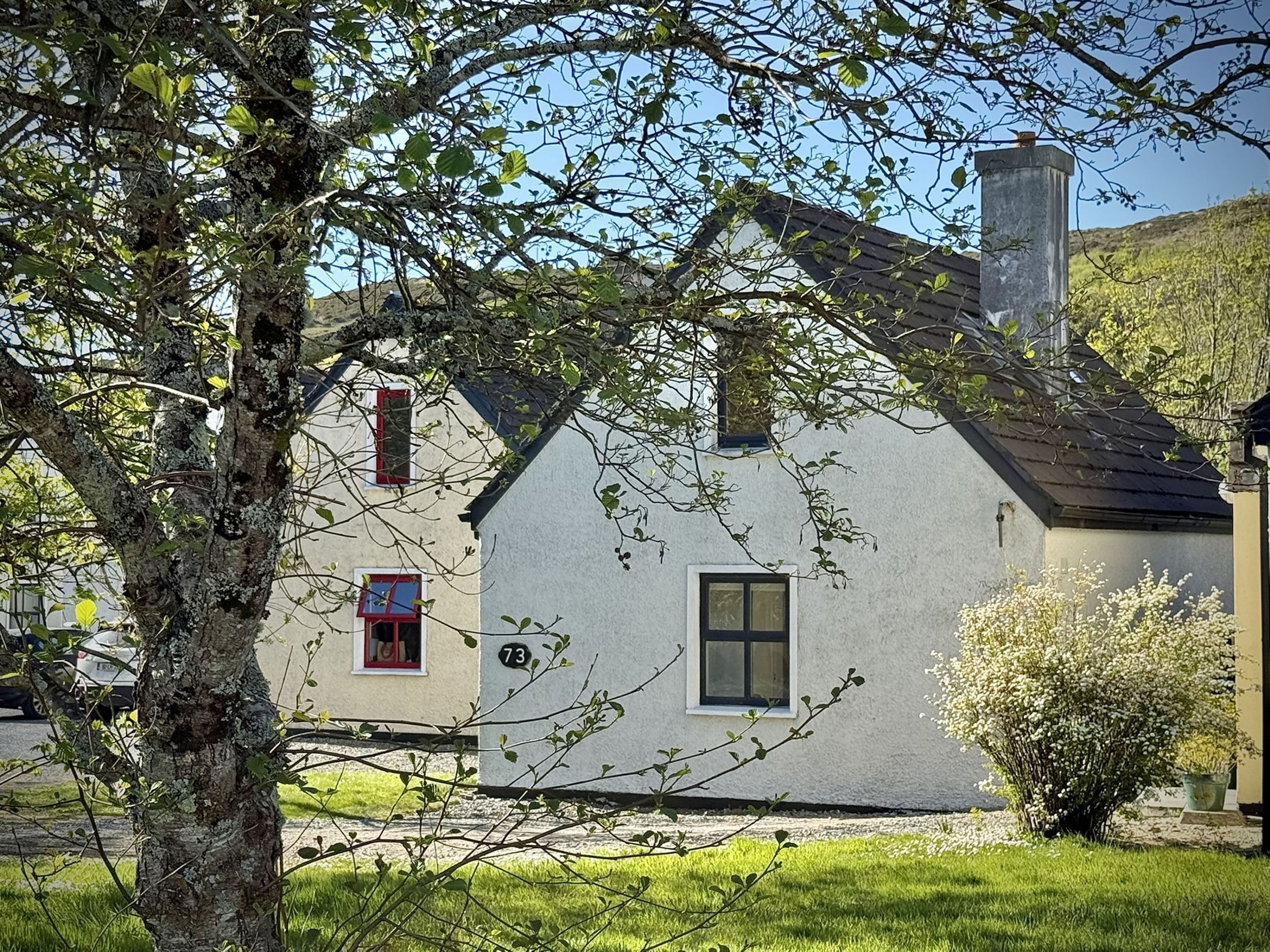 A white house with a red window, a chimney, and a number '73' on the wall.