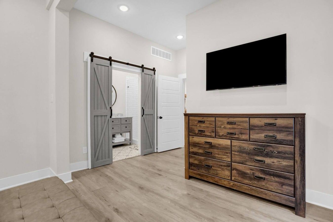 A room with a wooden dresser, a television mounted on the wall, and a sliding door leading to a bathroom.