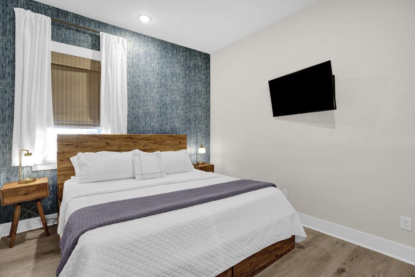 A hotel room with a bed, a television mounted on the wall, and a window with curtains.