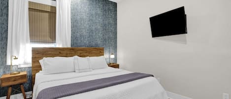 A hotel room with a bed, a television mounted on the wall, and a window with curtains.